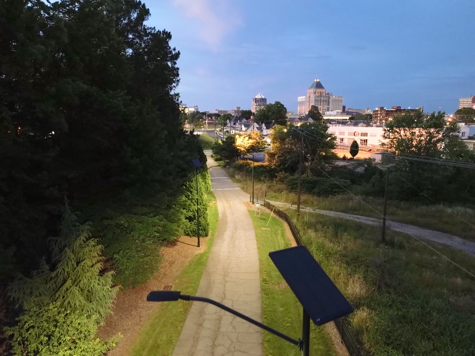 A civic greenway and surrounding city illuminated after dark
